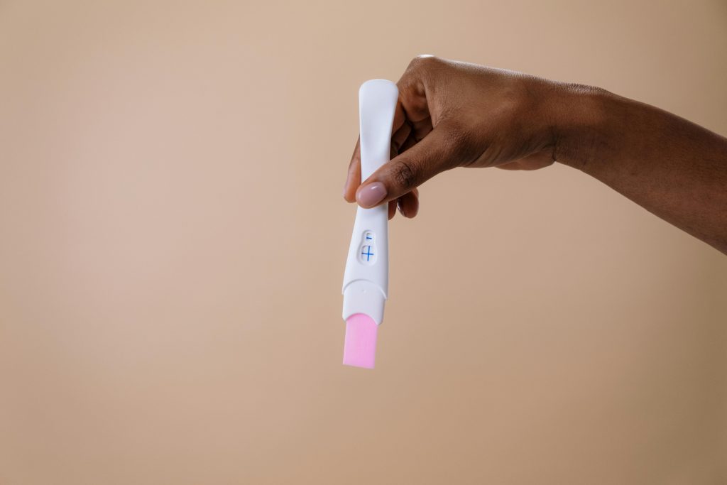 A woman's hand holding a positive pregnancy test on a neutral background.